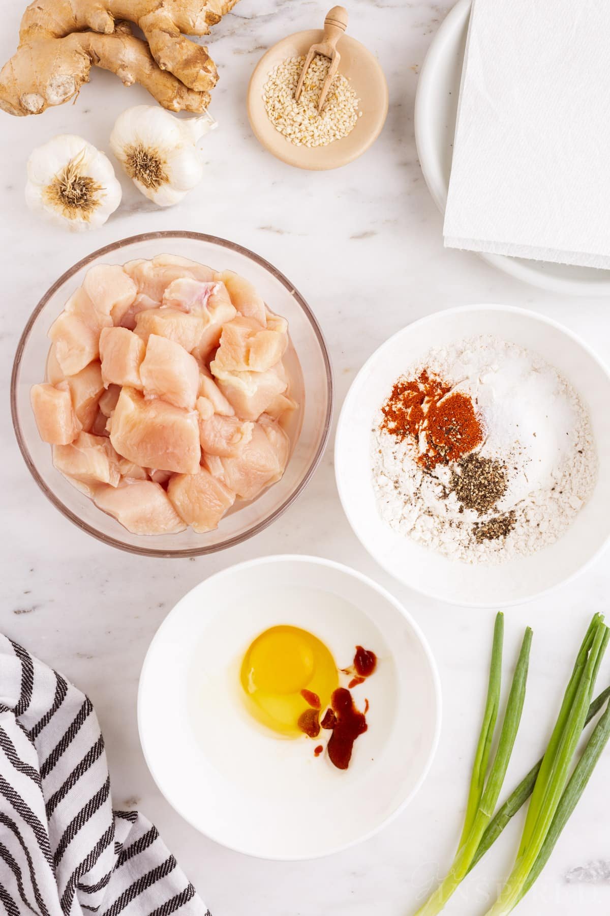 Dredging station with a bowl of cut chicken breast, bowl of spices and flour, bowl of buttermilk with egg and sriracha.