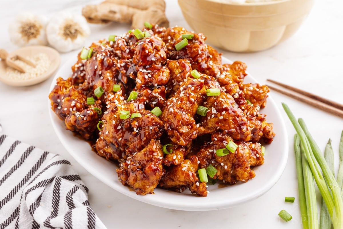 General Tso Chicken on a white plate, surrounded by recipe ingredients and a bowl of rice.