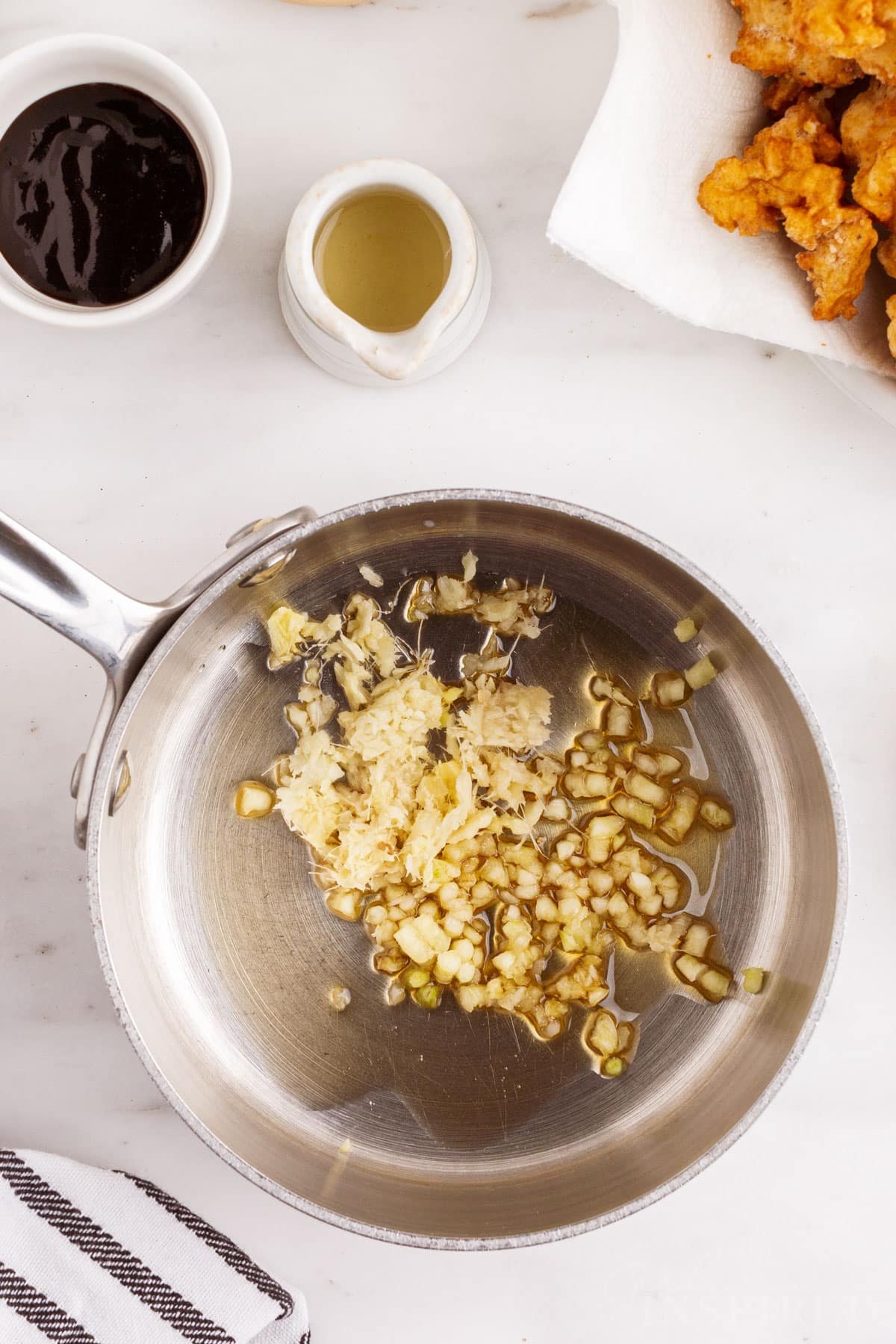 Pan with sesame oil, ginger, and garlic, plate with fried chicken pieces.