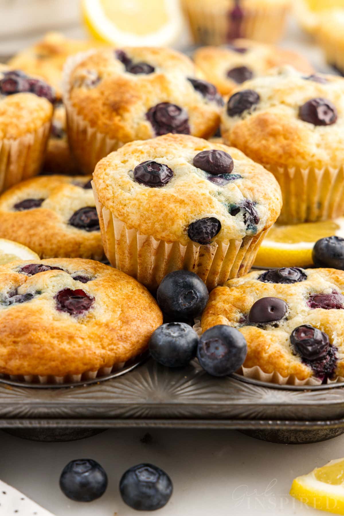 Lemon Blueberry Muffins in a muffin tin some stacked on the tin.