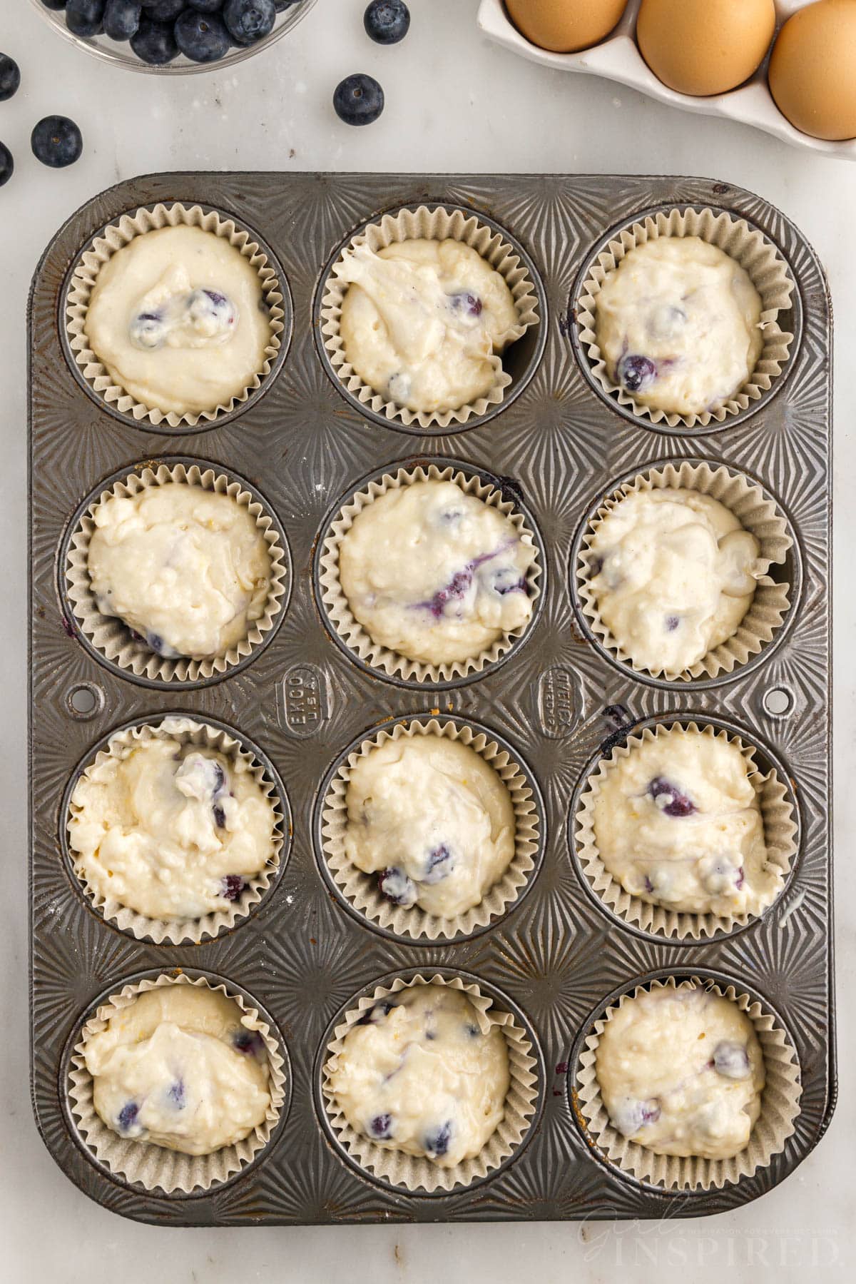 Muffin tin lined with papers filled with Lemon Blueberry Muffin batter.