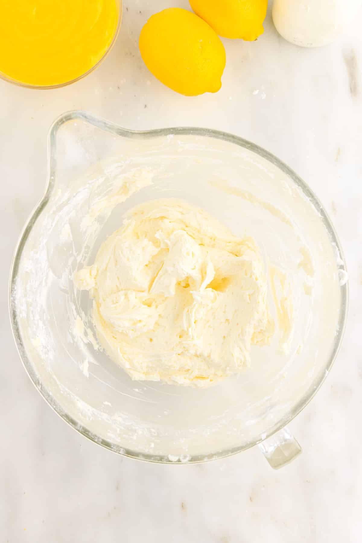 Lemon Buttercream Frosting in a mixing bowl next to lemons.