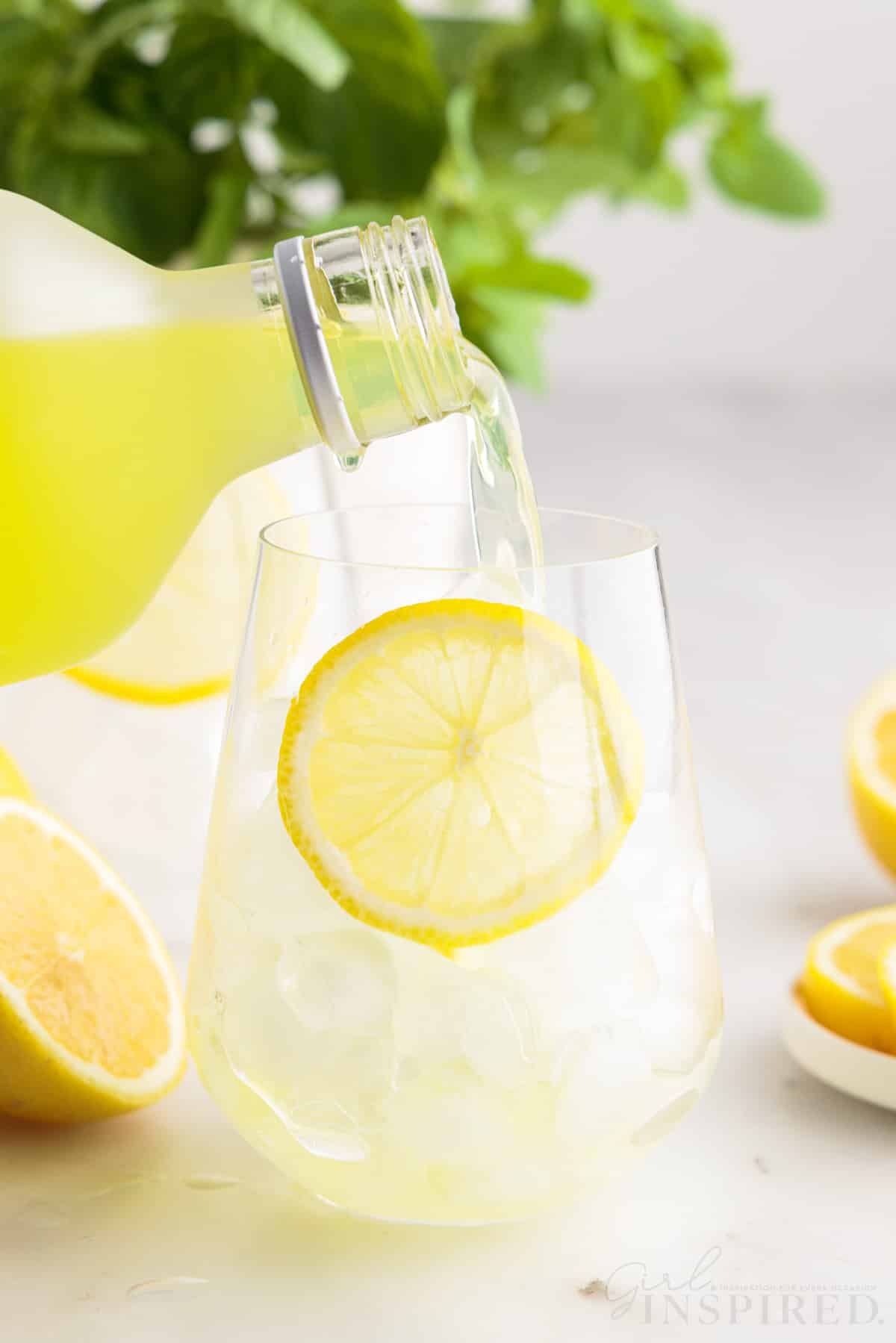 Limoncello being poured into a glass with ice and a lemon slice.