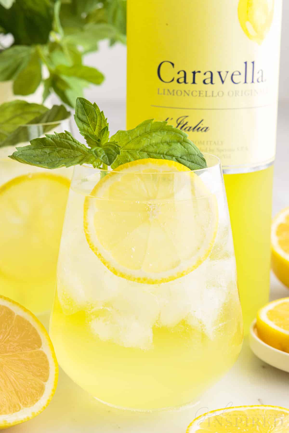 Close up of Limoncello Spritz with lemons and mint with a bottle of Limoncello in the background.