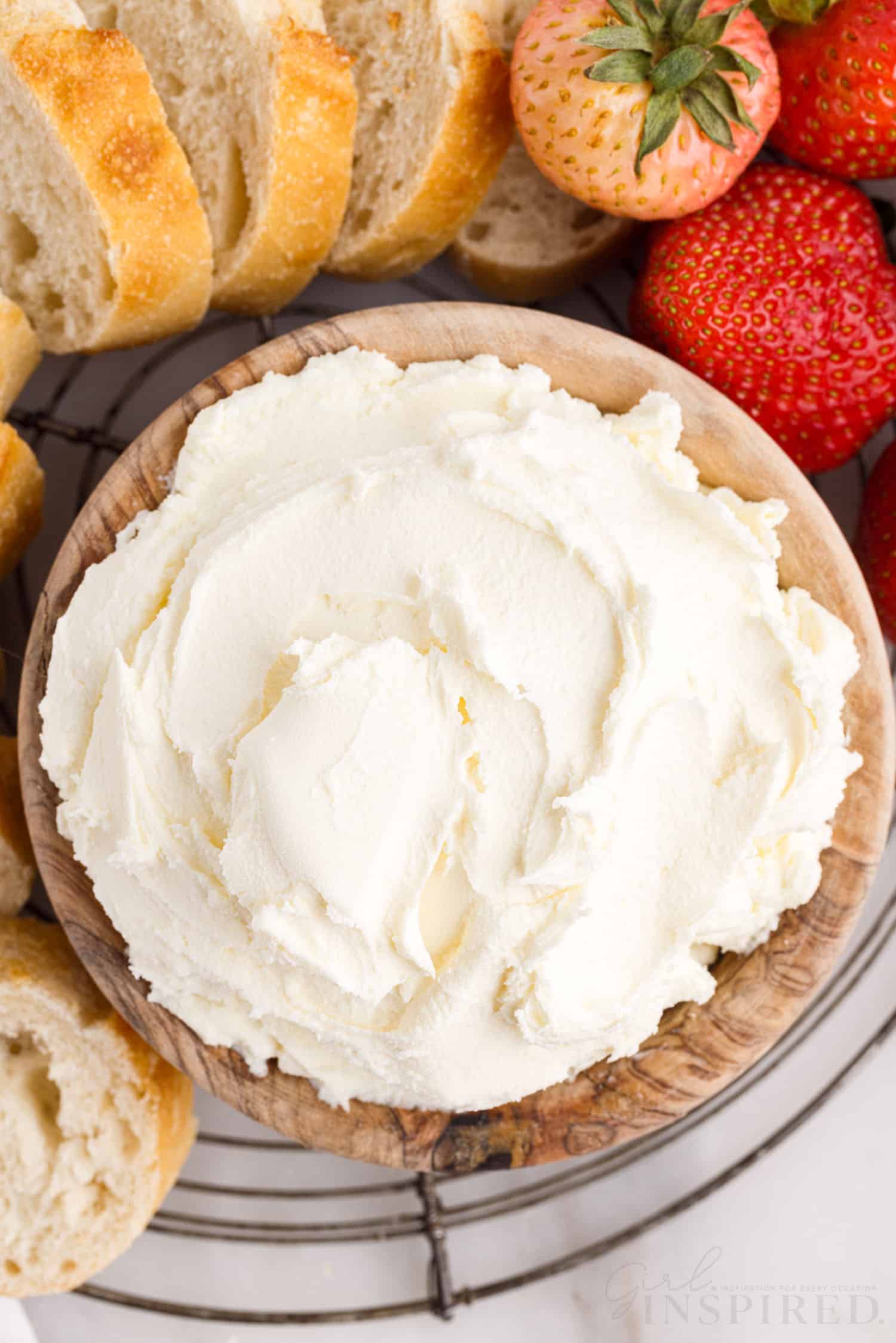 Overhead view of a dish of Mascarpone Cheese next to sliced bread and strawberries.