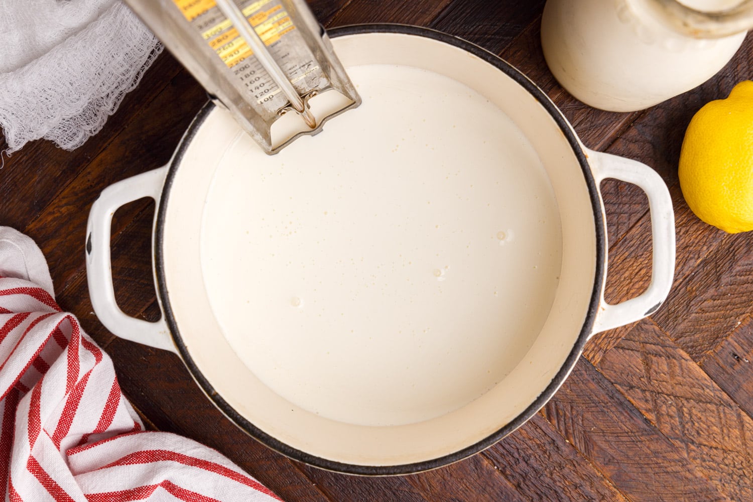 Monitoring the temperature of heavy cream with a candy thermometer in a Dutch Oven.
