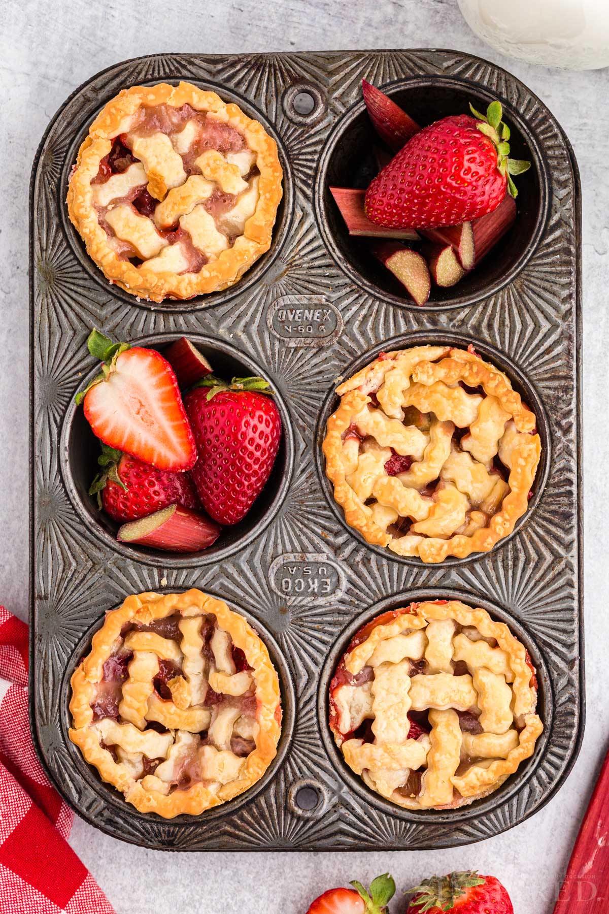 Mini strawberry rhubarb pies in a muffin tin and fresh strawberries filling some of the cavities.