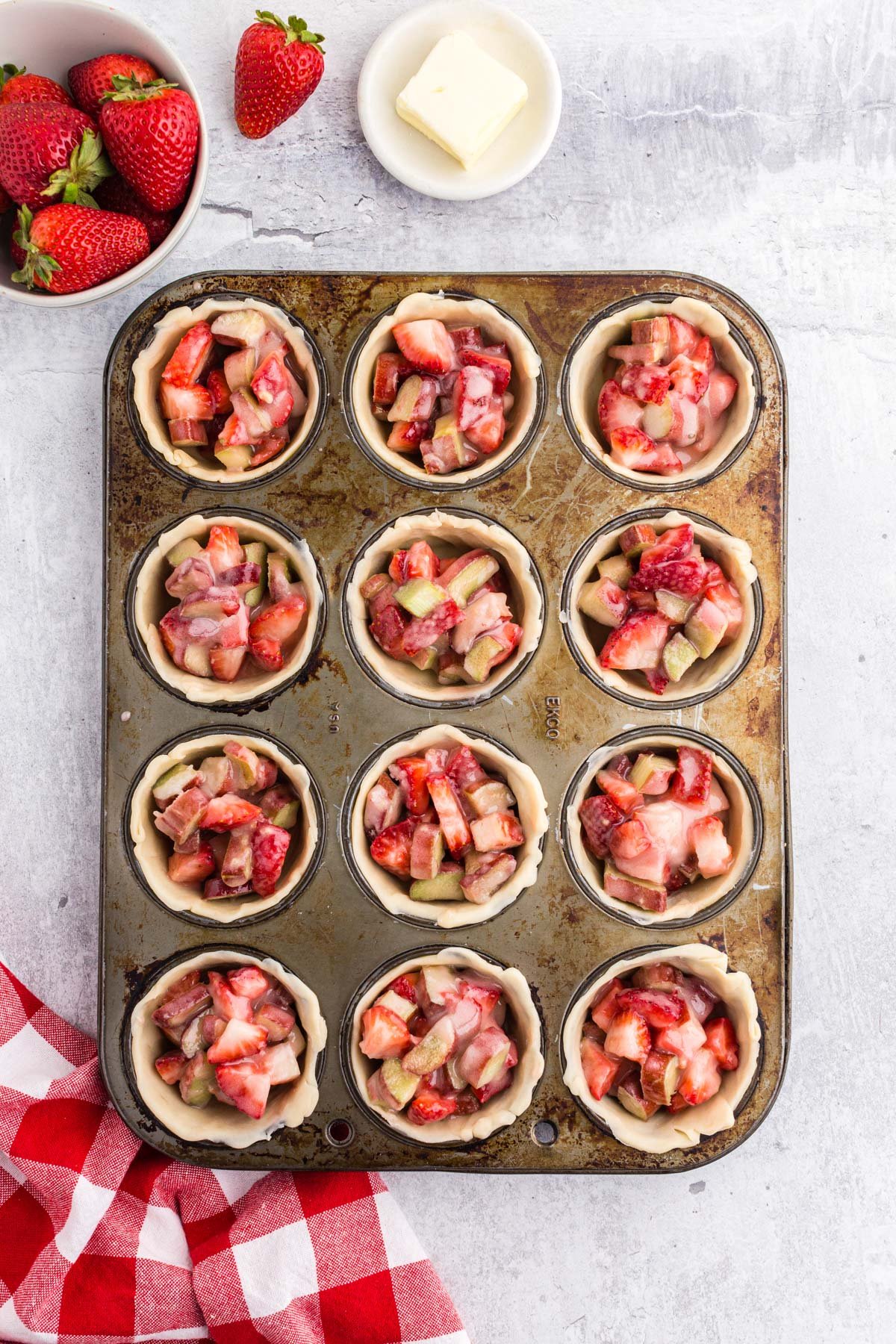 Strawberry rhubarb pie filling in each dough crust filling each cavity of a muffin tin. 