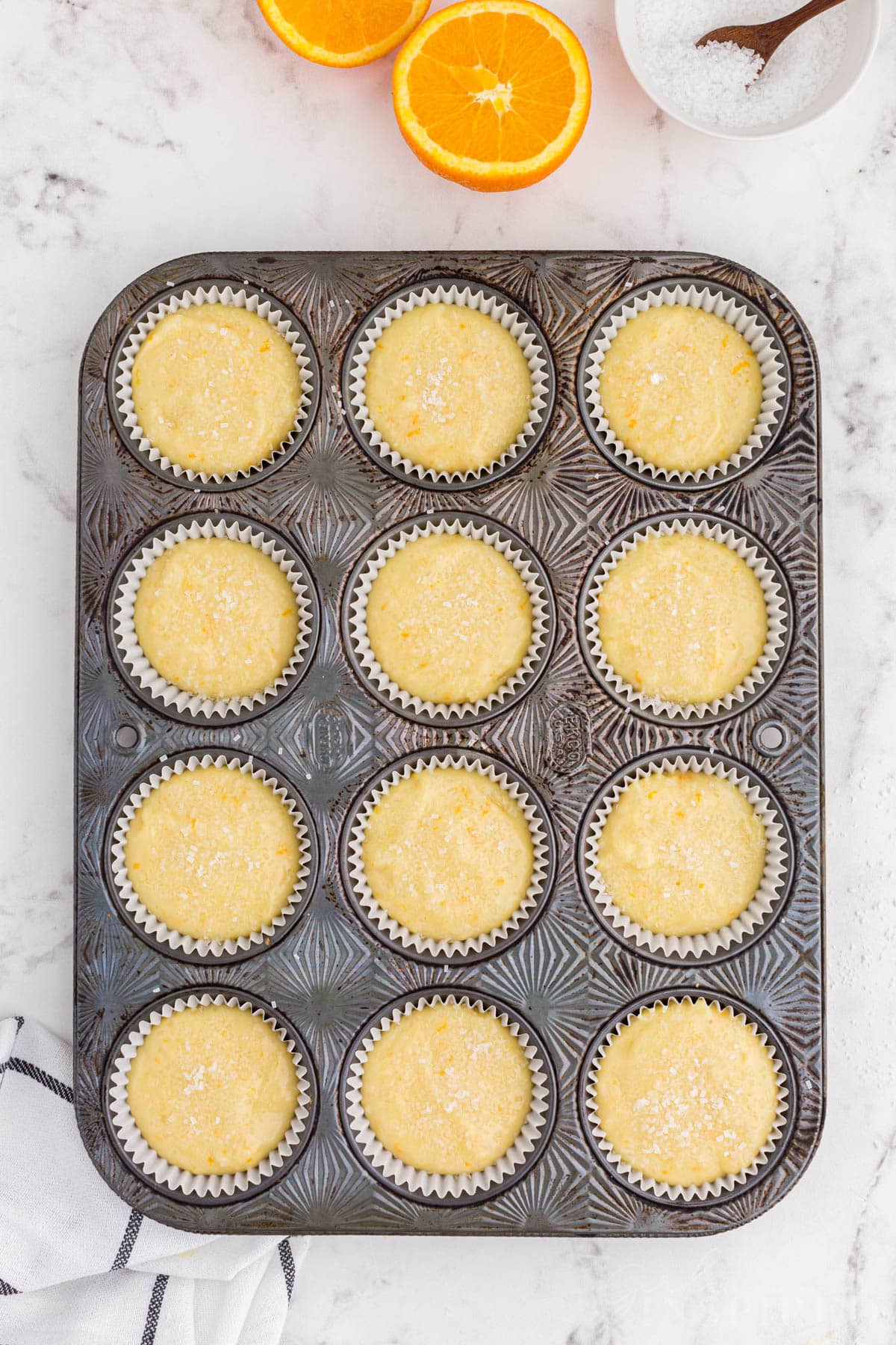 Muffin tray with orange muffin batter, coarse sugar sprinkled on the tops of the muffins.