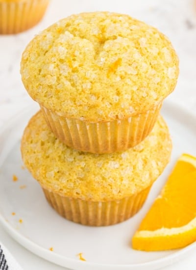 Two stacked orange muffins on a white serving plate.