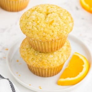 Close-up of two stacked orange muffins on a white serving plate.