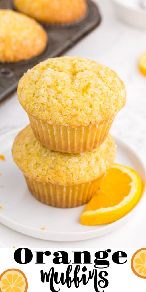 Two stacked orange muffins on a white serving plate, metal muffin tray with orange muffins in the background.