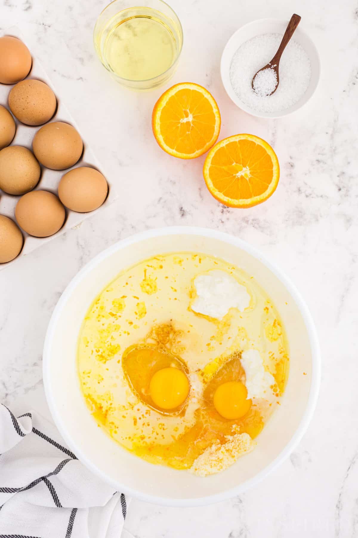 Large bowl with eggs, oil, buttermilk, orange juice, and orange oil, muffin ingredients on a marble countertop.