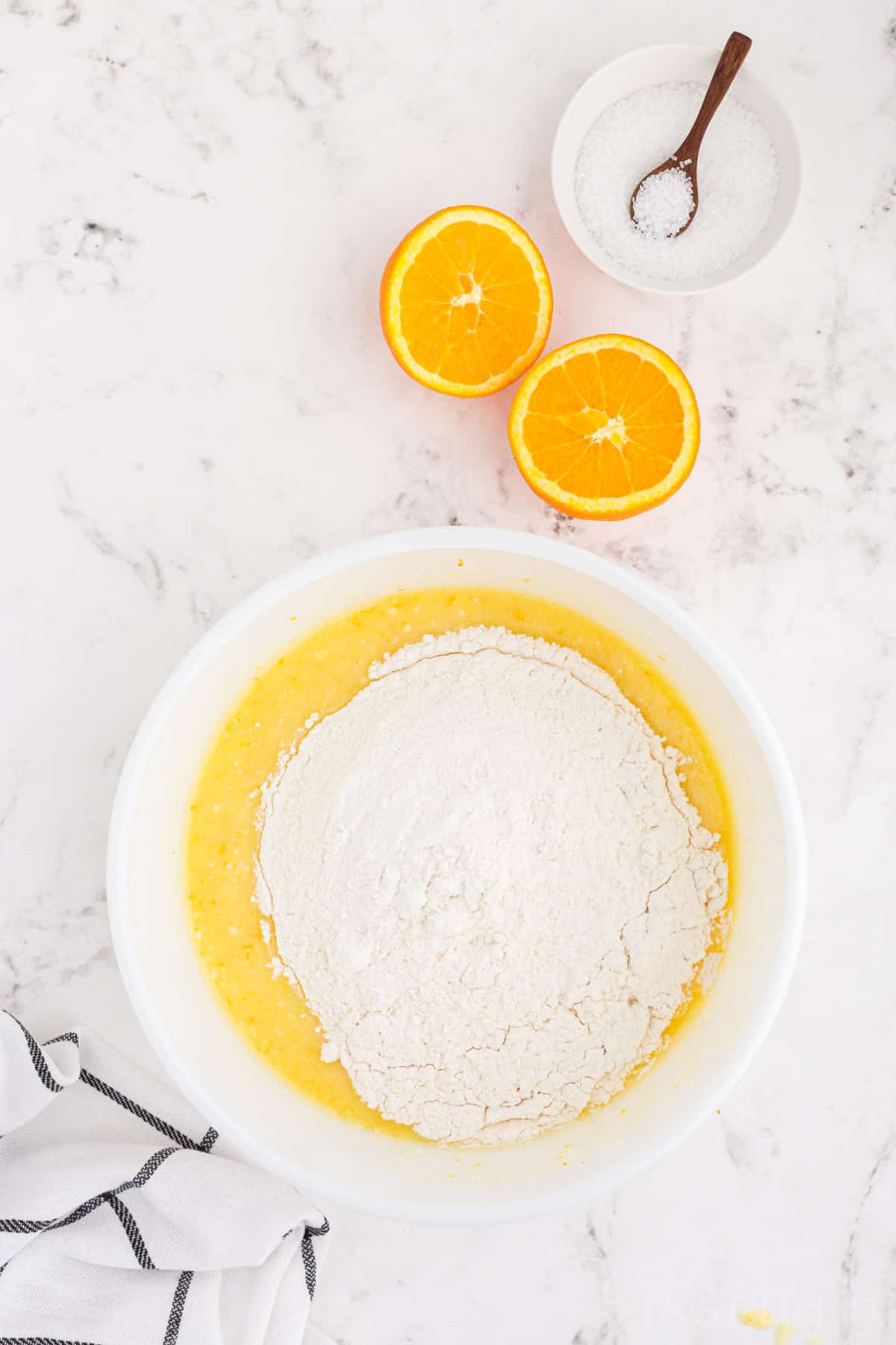 Large bowl with wet and dry orange muffin ingredients on a marble countertop.
