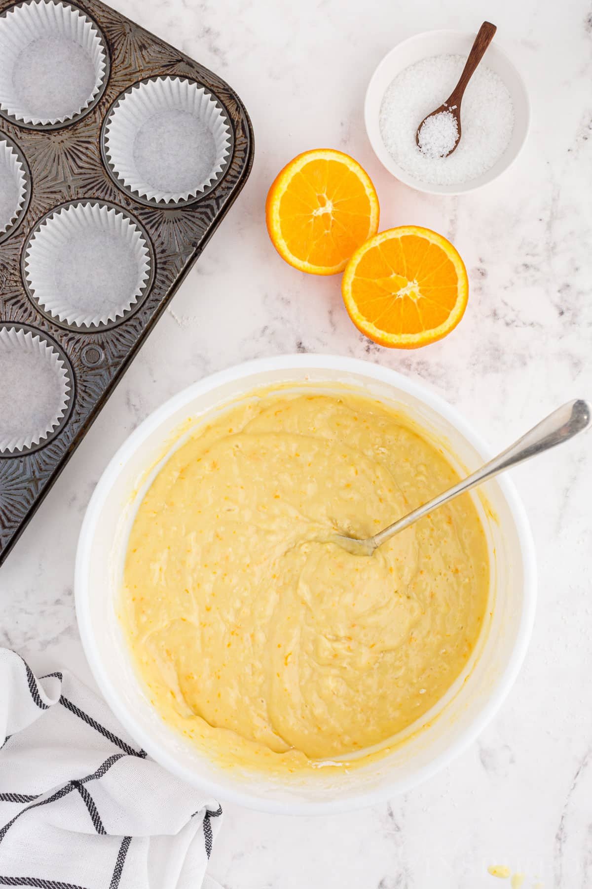 Large bowl with orange muffin batter, prepared muffin pan on a marble countertop.