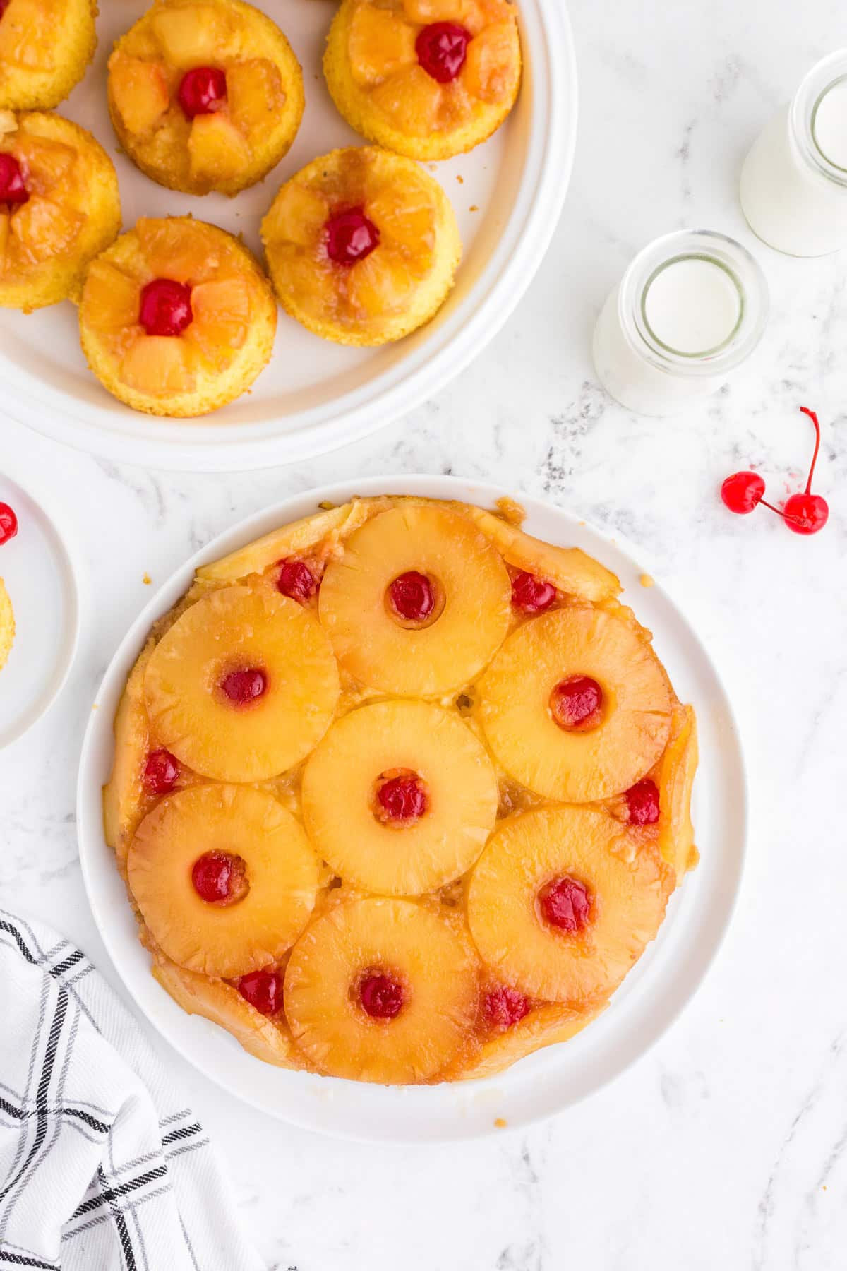 Overhead view of pineapple upside down cake and mini cakes on a white marble countertop.
