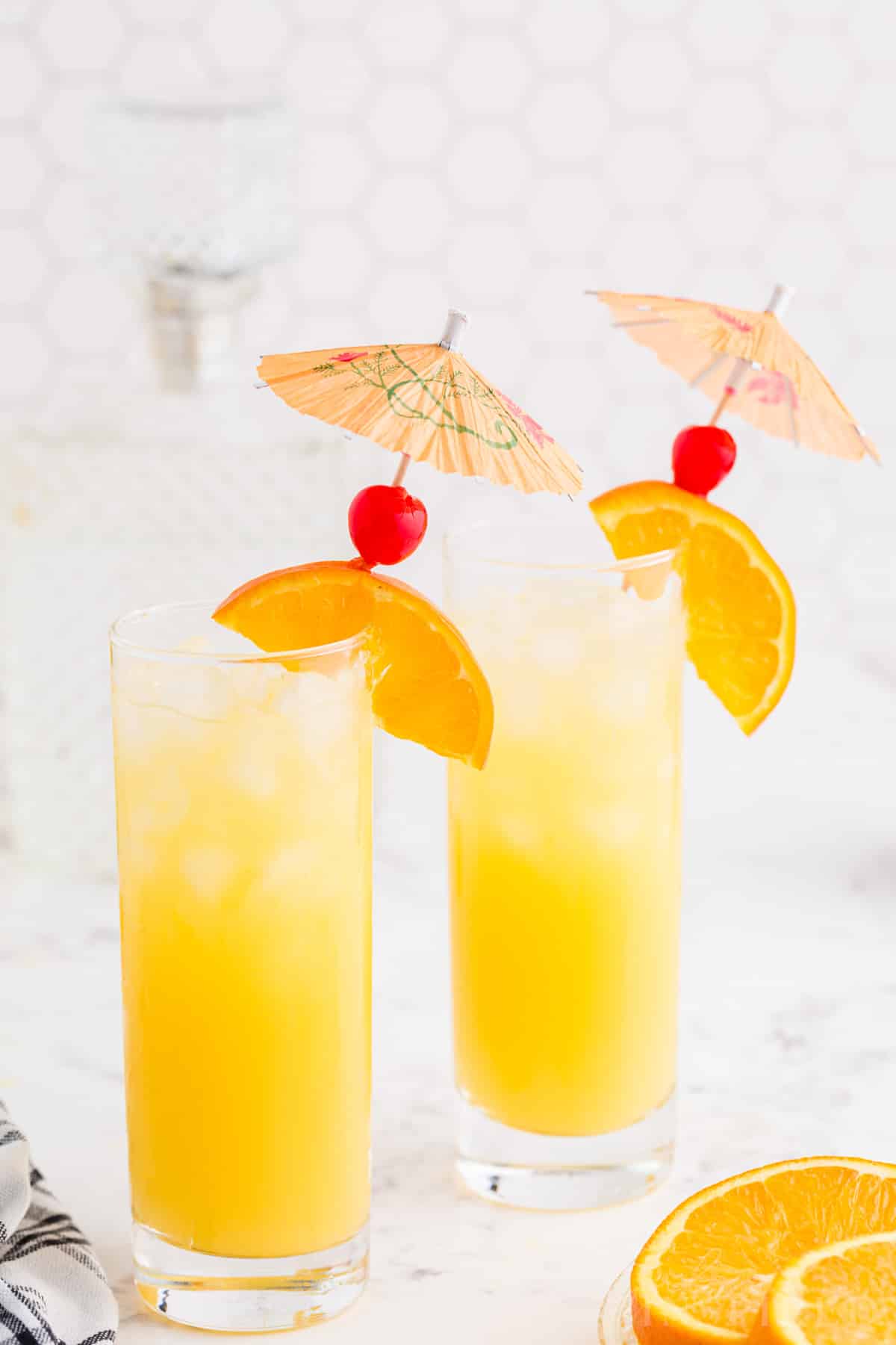Two glasses of screwdriver drink, garnished with orange slices and cherries.
