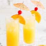 Two glasses of screwdriver drink with fruit garnish and decorative umbrellas.