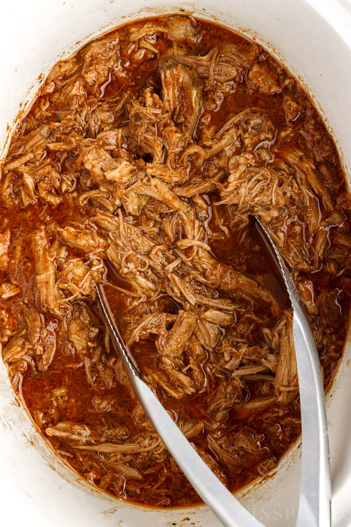 Tongs in Pork Barbacoa in a crock pot.