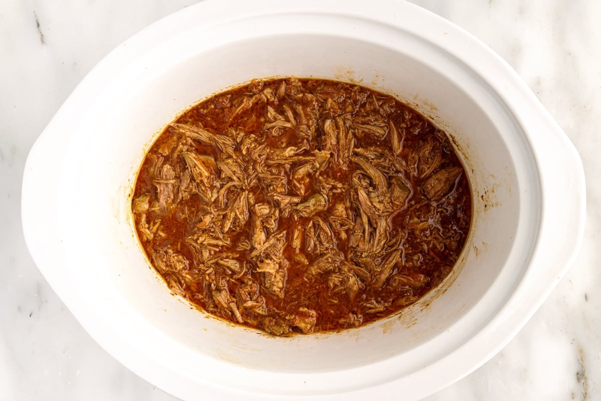 Meat is placed in sauce in crock pot after being shredded.