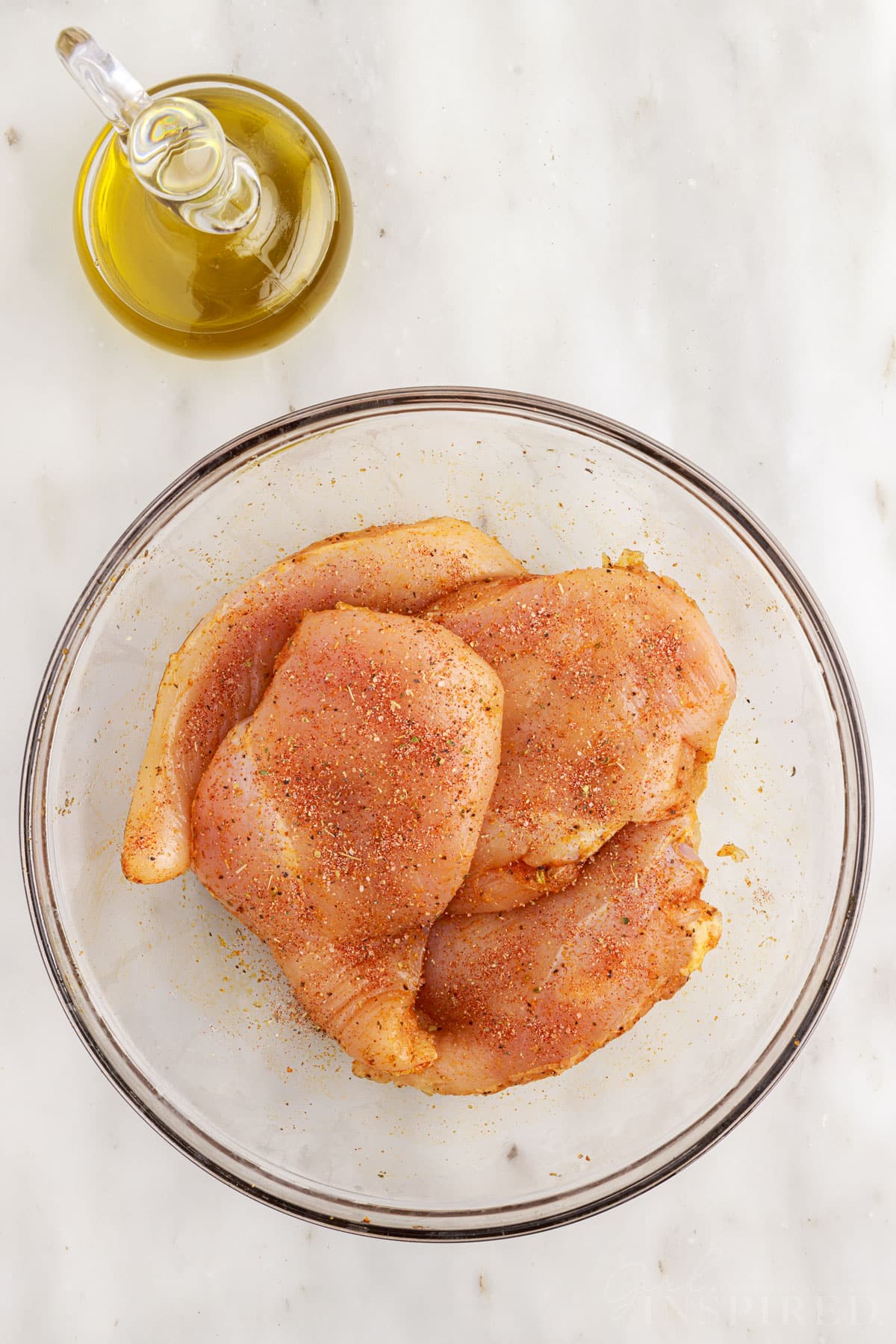 Air Fryer Boneless Chicken Breasts covered with oil and seasonings in a mixing bowl.
