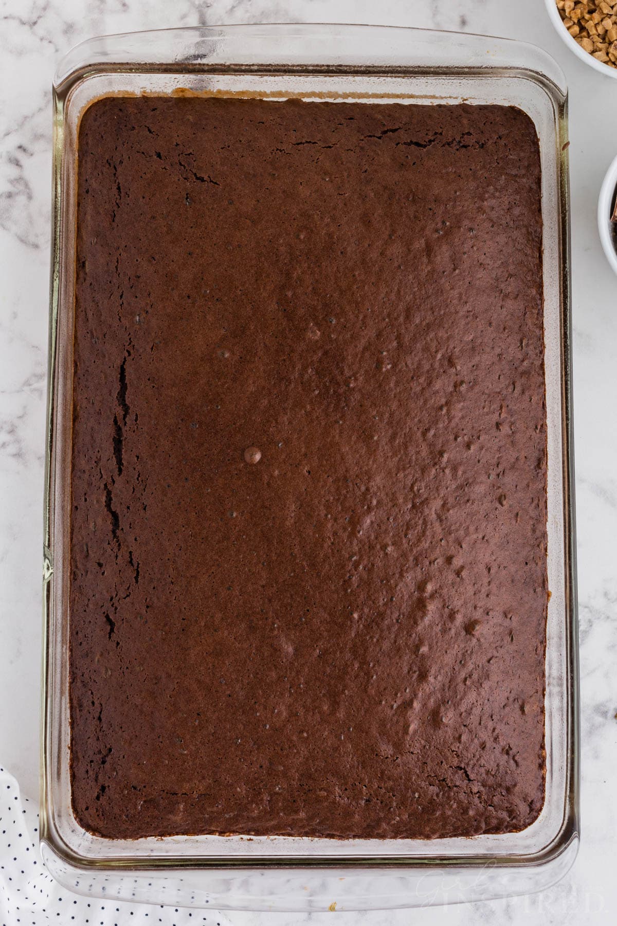 Baked chocolate cake base in a glass baking dish on a countertop. 