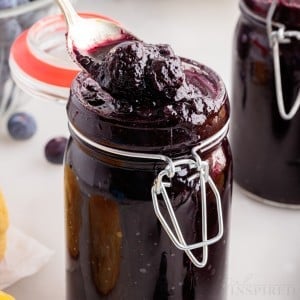 A mason jar filled with Blueberry Butter, a spoon lifting some out.