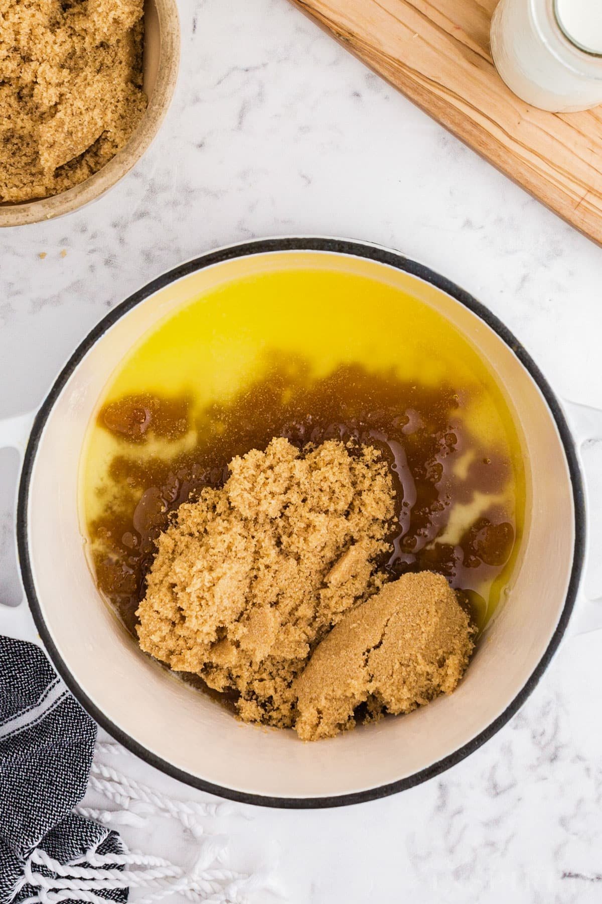 Saucepan with melted butter and brown sugar, brown sugar caramel sauce recipe ingredients surrounding the saucepan.