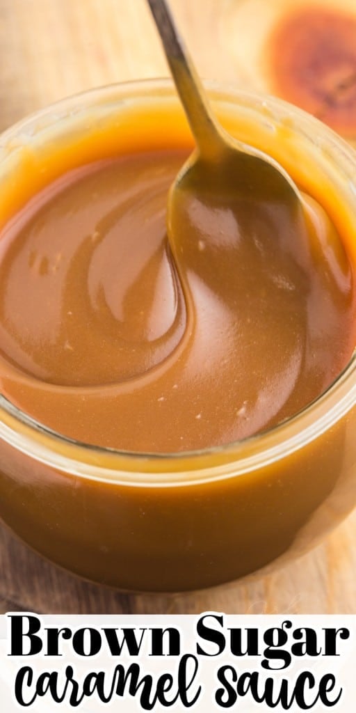 Close up of brown sugar caramel sauce in a glass jar with metal spoon on a wooden kitchen board.