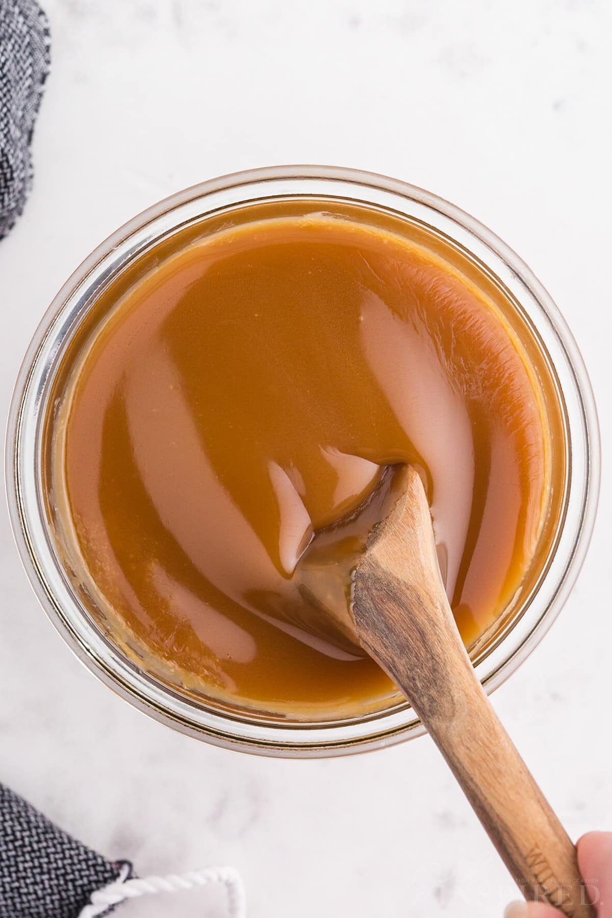 Overhead view of brown sugar caramel sauce in a glass jar with wooden stirring spoon.