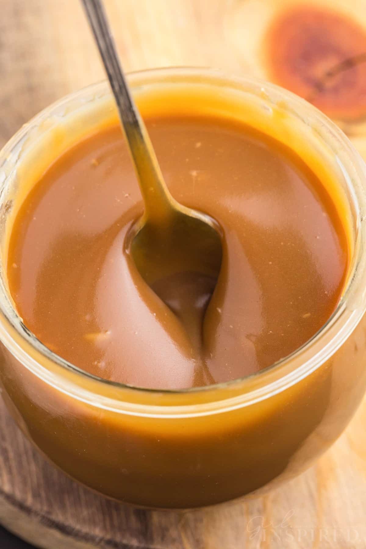 Brown sugar caramel sauce in a glass container with a metal teaspoon. 