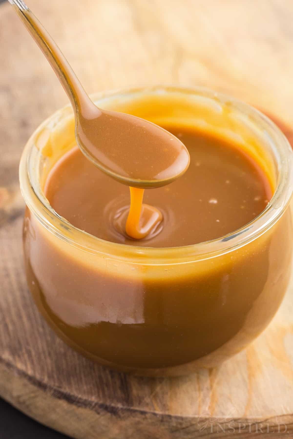 Brown sugar caramel sauce in a glass jar on a wooden kitchen board.