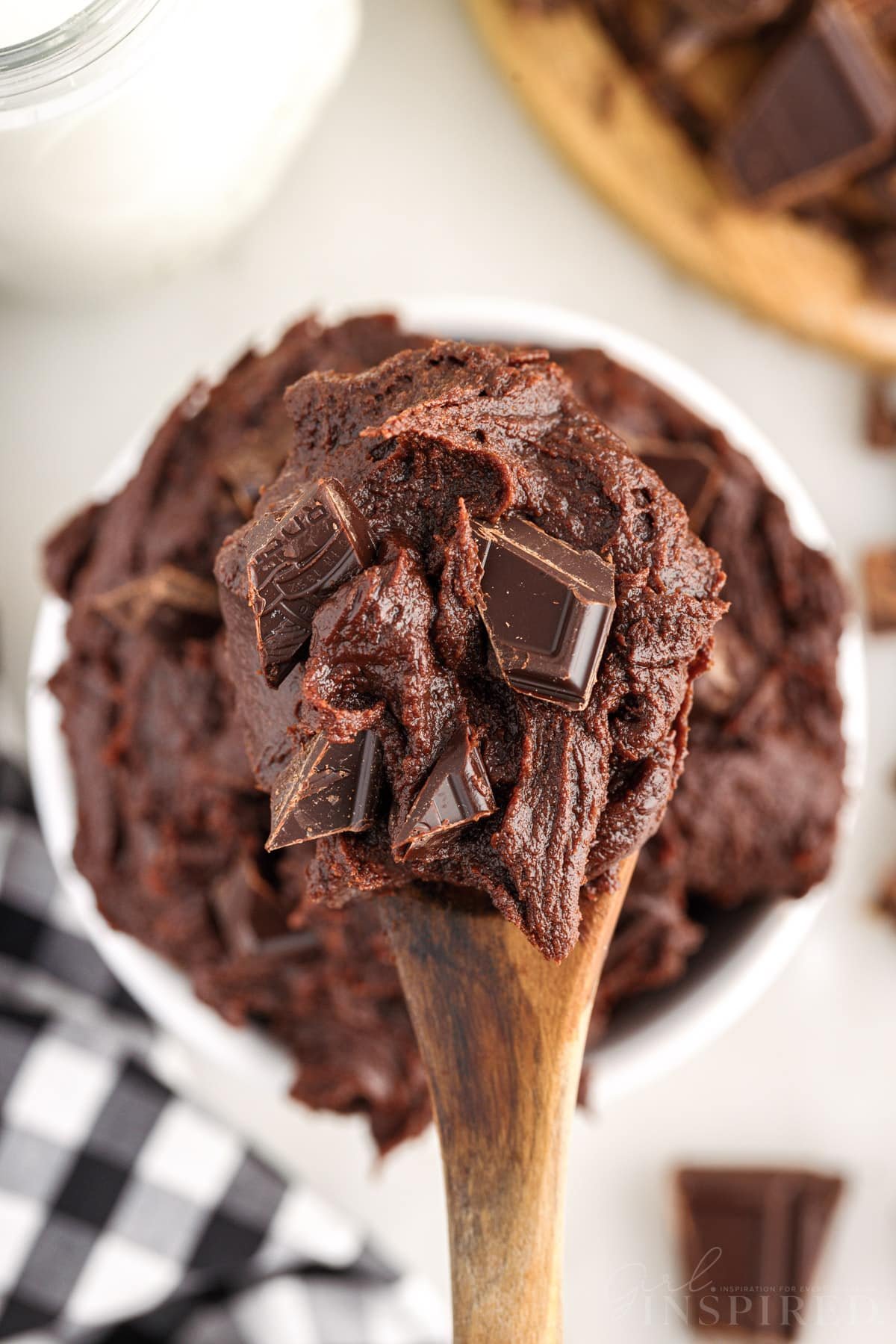 A wooden spoonful of Edible Brownie Batter over a serving bowl of it.