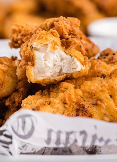 Close up of buttermilk fried chicken tenders with a bite taken from one piece.