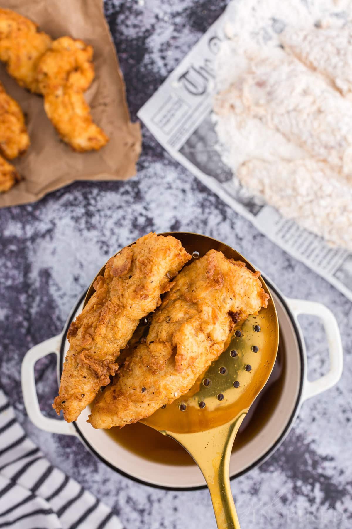 Slotted spoon above Dutch oven with freshly fried buttermilk fried chicken cutlets, parchment paper with freshly fried chicken cutlets, raw chicken cutlets coated with buttermilk and flour mixture on parchment paper.