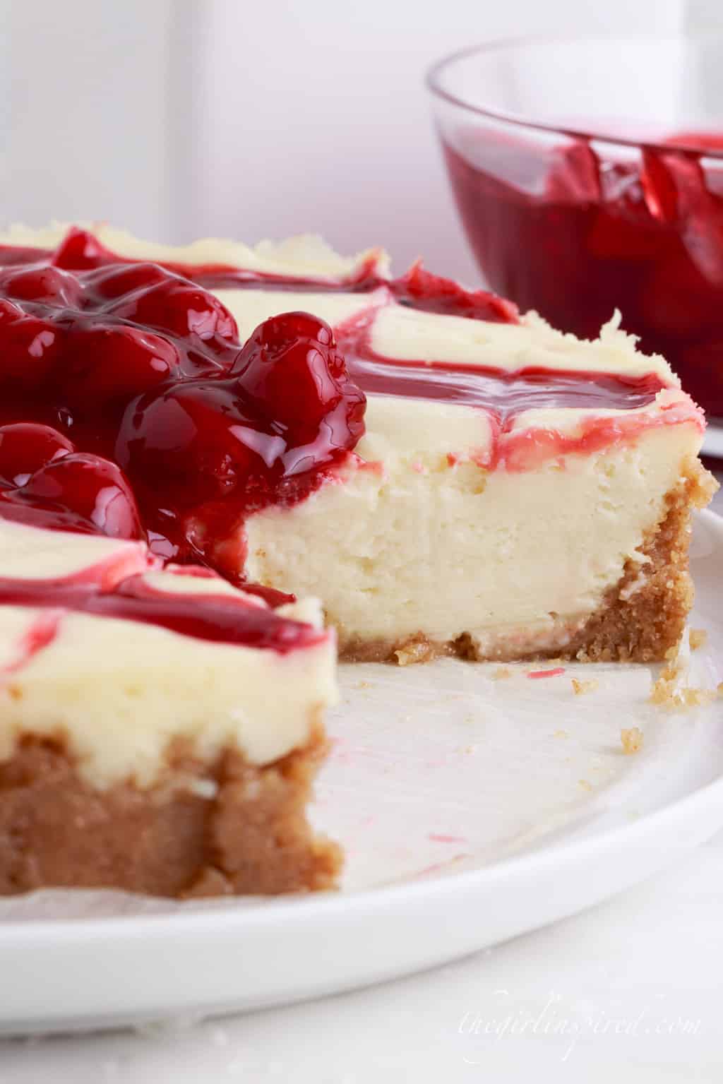 A Cherry Cheesecake with a slice missing from it.