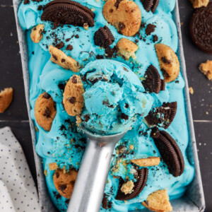 Ice cream scoop with a big scoop of blue cookie monster ice cream on top of loaf pan filled with ice cream.