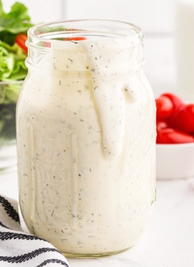 Close up of Hidden Valley Ranch Dressing in a mason jar a salad and tomatoes in the background.