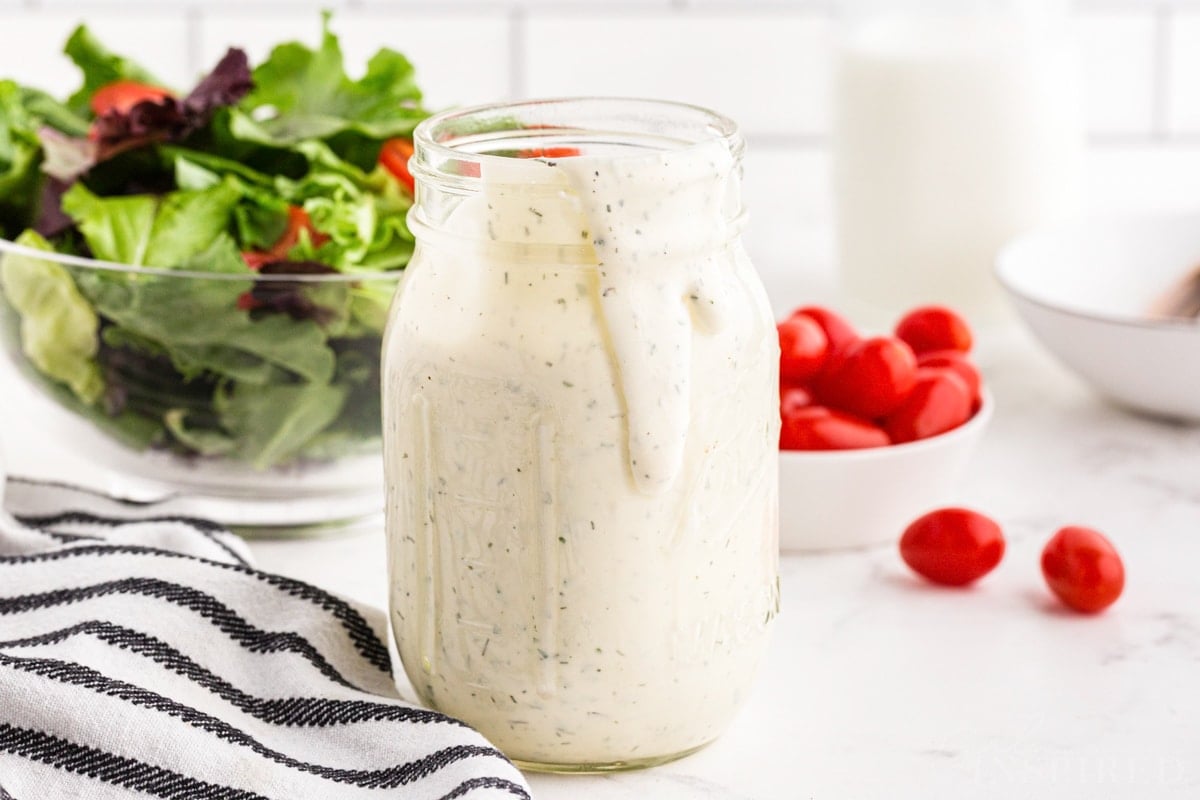 Hidden Valley Ranch Dressing Recipe in a jar with a salad and tomatoes in the background.