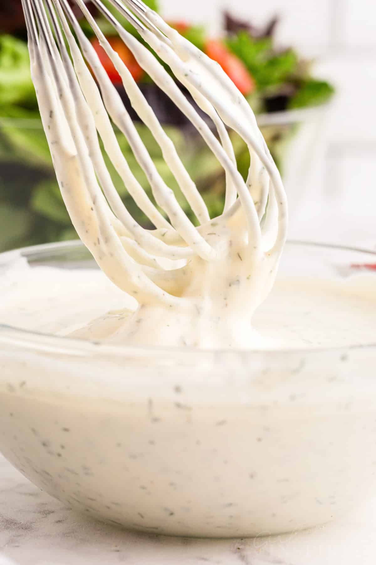 Front close up of a whisk lifted out of Hidden Valley Ranch Dressing covered in dressing.