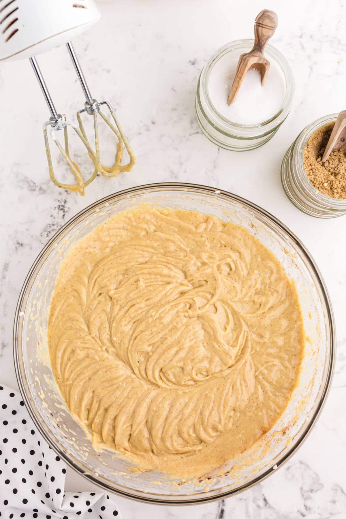 Fully beaten and smooth crack cake batter in a mixing bowl, hand mixer and recipe ingredients placed around the bowl.