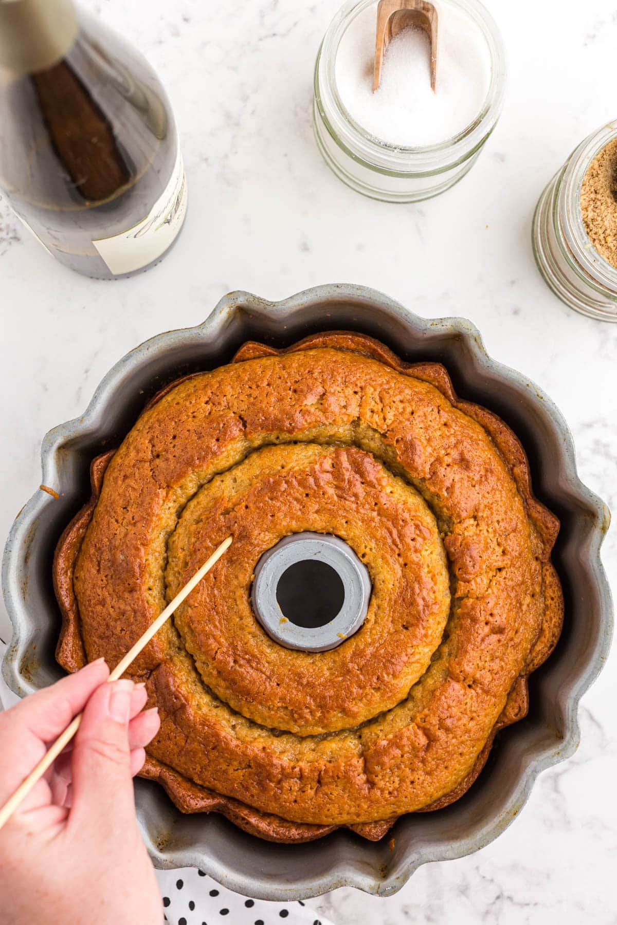 Hand with skewer poking holes in the top of the baked crack cake.