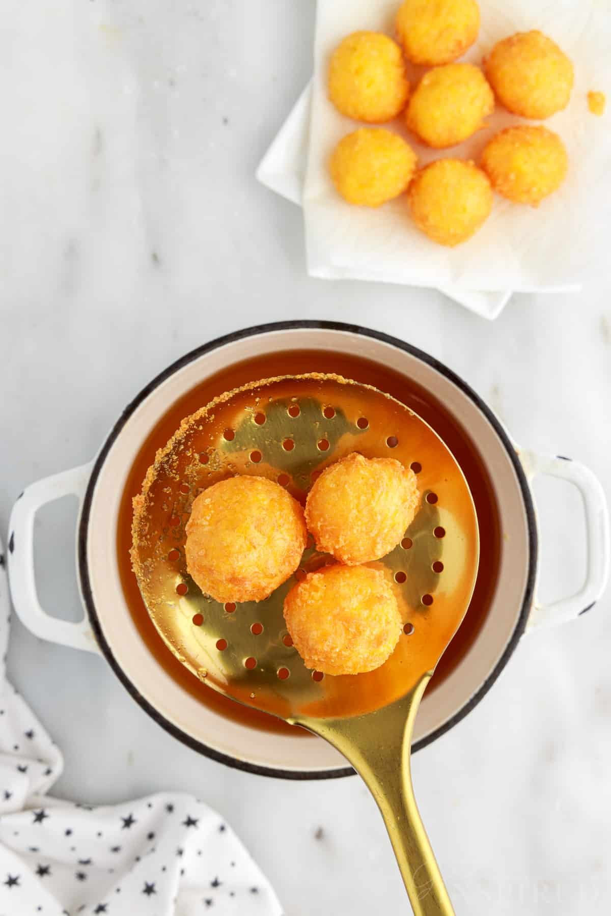 A slotted spoon lifting out three Fried Cheese Balls.