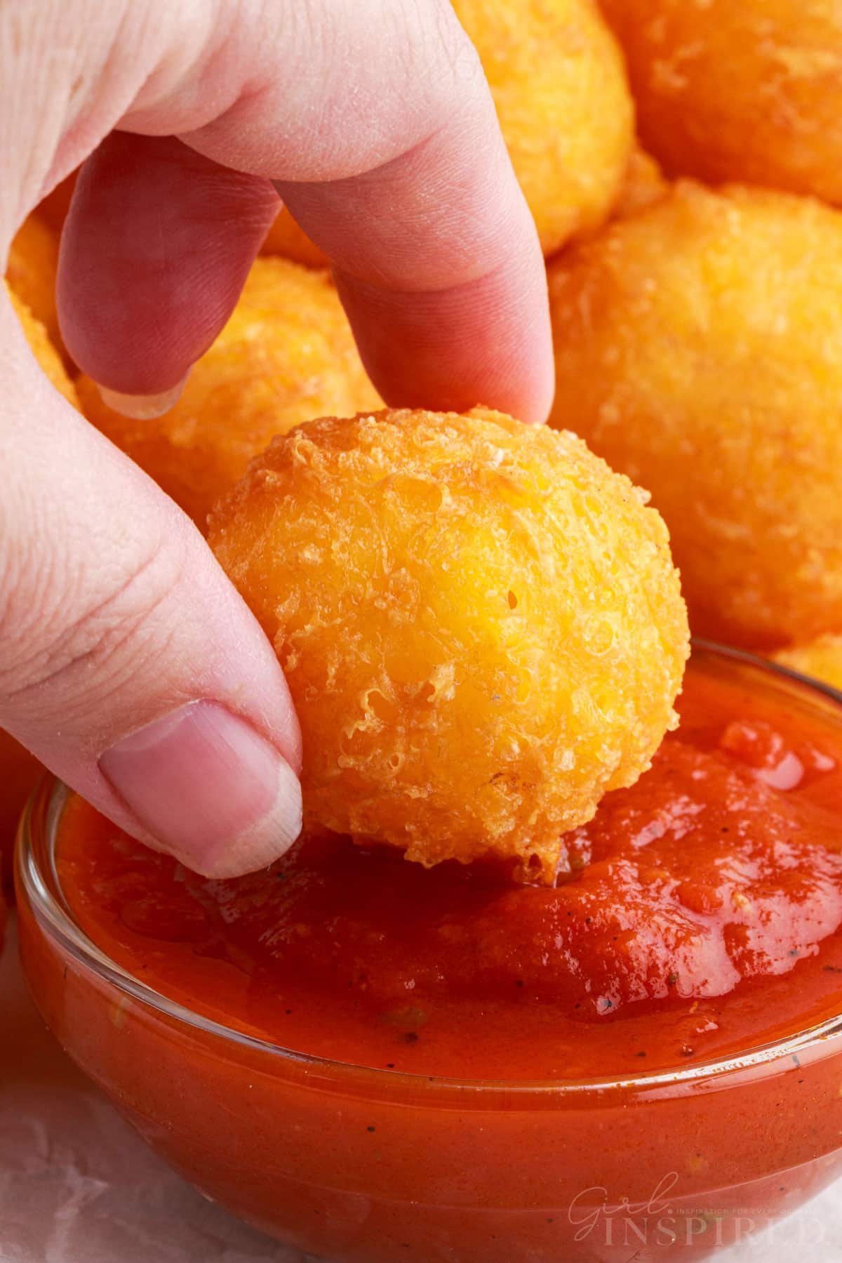 A Fried Cheese Ball being dipped in sauce.