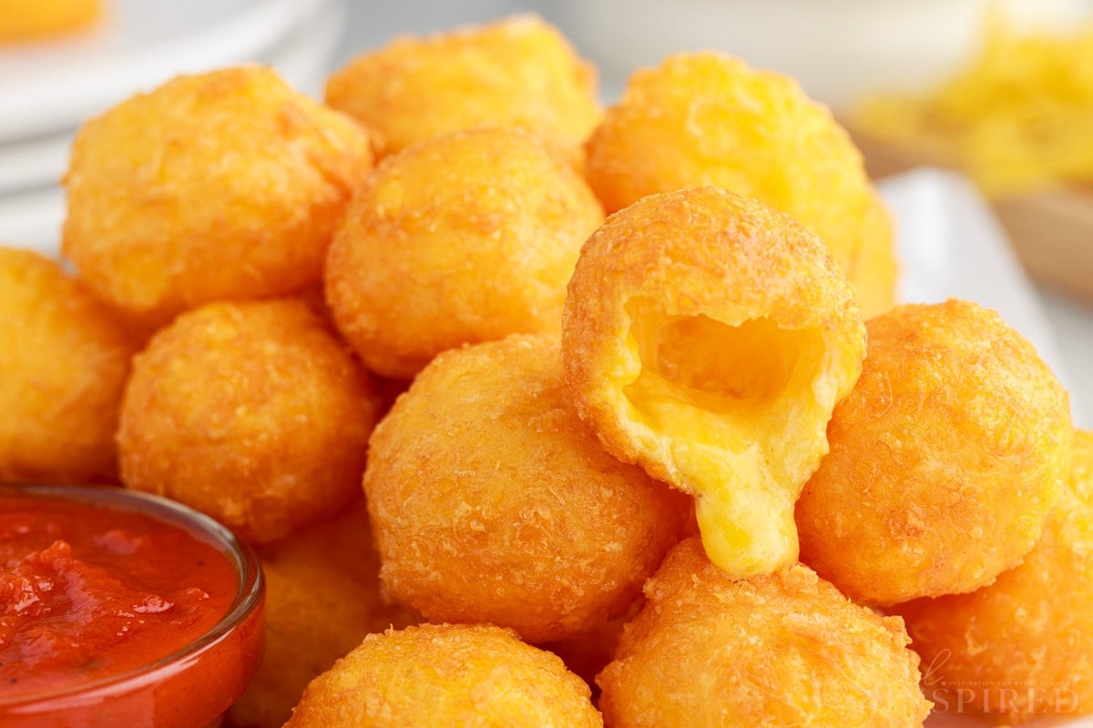 Fried Cheese Balls on a plate next to sauce one ball cut open.