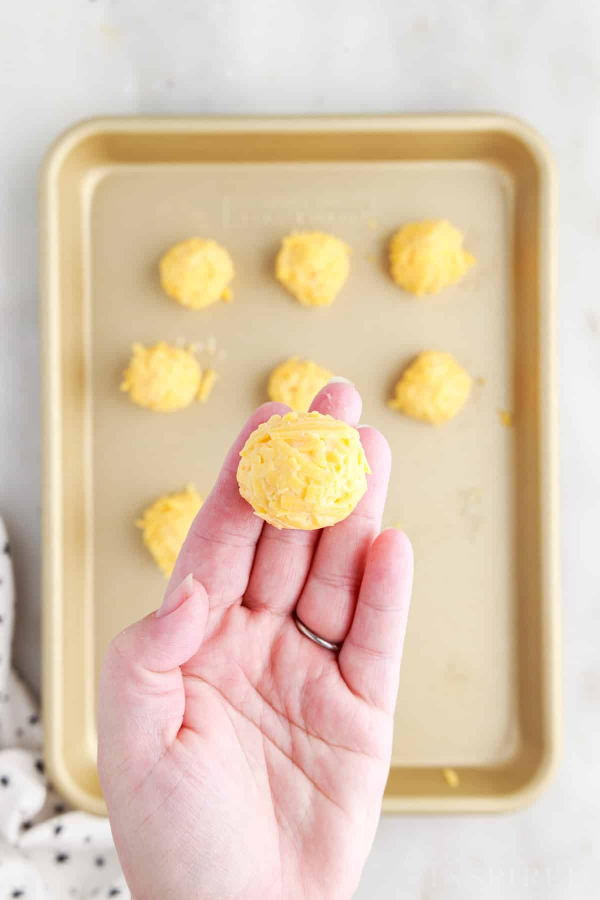 Fried Cheese Ball being held above a cookie sheet full of them.