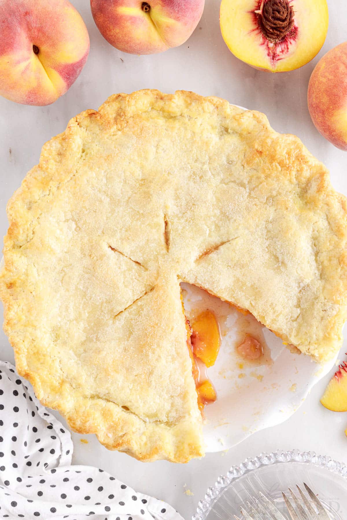 A slice missing from the Fresh Peach pie with peaches in the background.