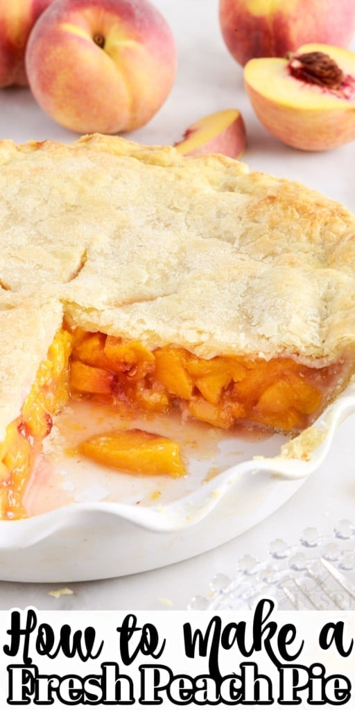 Front view of a peach pie in a white baking dish with a big slice removed from it and peaches lying around in the background