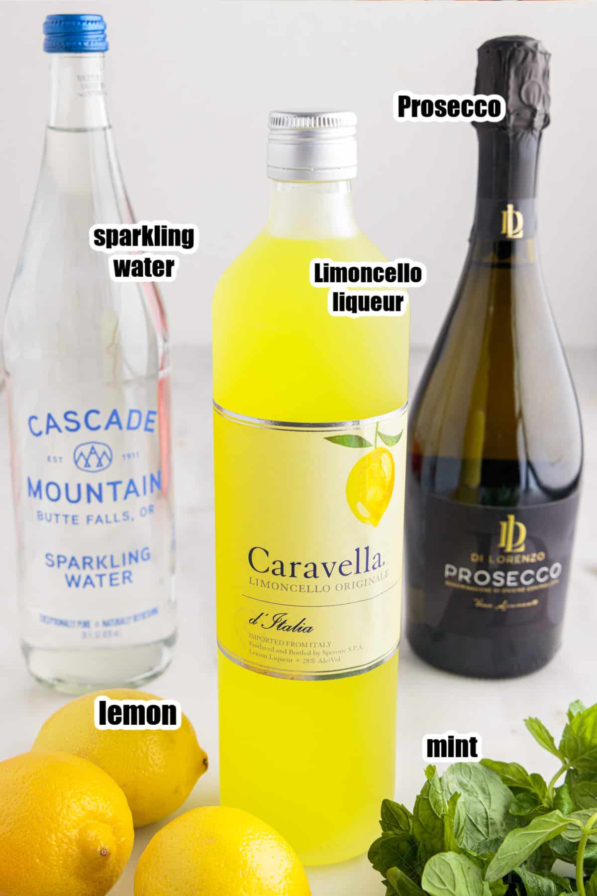 Sparkling water, Prosecco, and Limoncello bottles with mint and lemons in front of them.