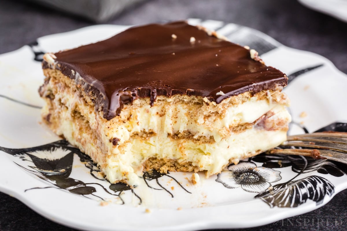 Close up of no bake eclair cake with forkful removed on a white serving plate.
